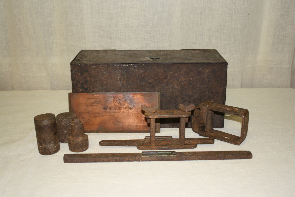 A printing plate and various forger's tools arranged in front of an iron box.