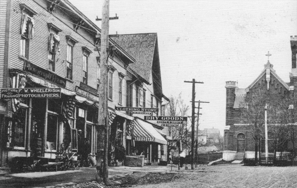 In the foreground we can see the sign indicating photographer Frank Wheeler's studio. His neighbours on this commercial street in Richford include clothing and fabric stores.