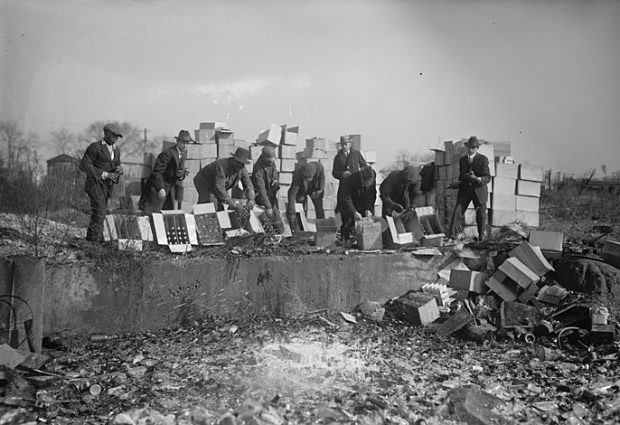 Officers throw bottles and crates of beer and alcohol into a pit.