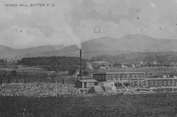 In the foreground is Sutton’s Veneer Mill plywood factory on Western Street and its log-filled lumber yard; in the background, the Sutton Mountains.