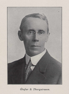 Svarthvít ljósmynd af miðaldra manni, tekin frá herðum og upp. Hann er með gleraugu og klæddur í jakkaföt og bindi.