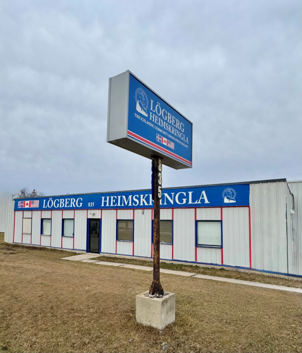 A color photo of a modern, single-story building with a sign that reads Lögberg Heimskringla: The Icelandic Community Newspaper in English. Flags of Iceland and Canada are on display above the entrance at 835 Marion Street.