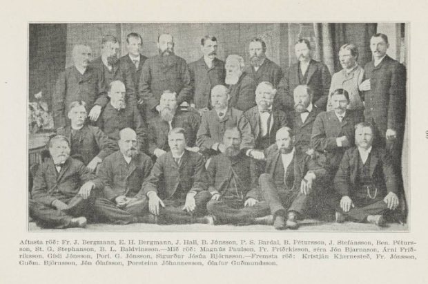 Photographie en noir et blanc d’un groupe de 30 hommes posant en trois rangées, vêtus de costumes formels du 19e siècle. Certains hommes sont assis en pose tailleur par terre au premier rang, d’autres sont assis sur des chaises au centre, et la rangée arrière est debout. La plupart portent une moustache ou une barbe, et leurs expressions sont sérieuses. Sous l’image figure une légende en islandais énumérant les noms de tous les individus sur la photo, dont Fr. J. Bergmann, St. G. Stephanson et Ólafur Guðmundsson. L’arrière-plan montre un rideau uni. 