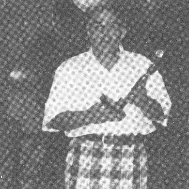 Black and white photograph of a man holding a trophy in his hands, wearing a white shirt and checkered pants.