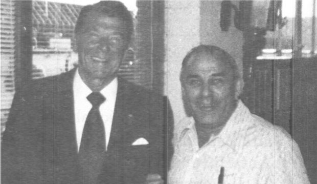 Black and white photograph of Normand Houle wearing a black-striped shirt, with Ronald Reagan in a dark suit, white shirt, and dark tie. Both are smiling.