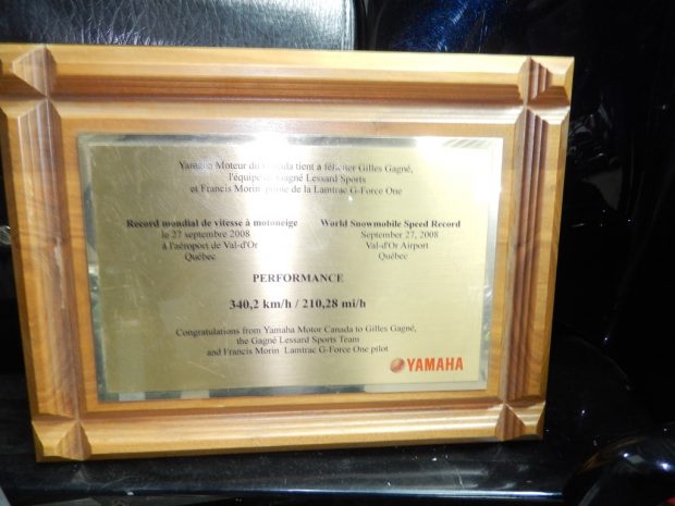 Colour photograph of a khaki-coloured plaque award with red and black engraved lettering, framed in wood.