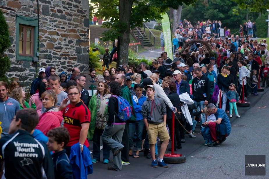 Colour photo of people standing in a long line to see Foresta Lumina, waiting in front of an old brick building located at the entrance of the Coaticook Gorge park.