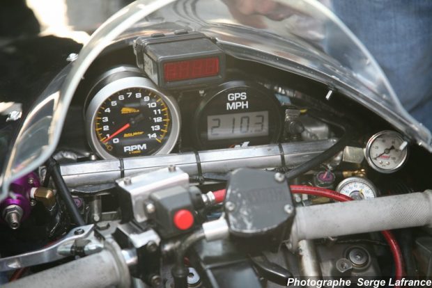 Colour photograph showing a closeup of the handlebars of a snowmobile, and various dials and screens on the dash protected by a raised piece of molded plastic.