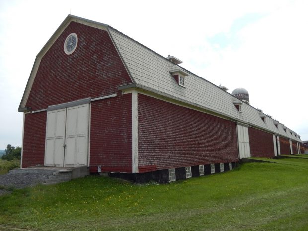 Colour photgraph showing the full length of the barn at Ferme-du-Plateau. The building is burgundy-coloured with white doors.