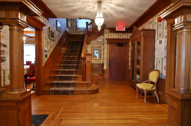 Colour photograph of the entrance hall of the Beaulne Museum. The photo highlights furnishings and woodwork, as well as a wide, carpeted staircase at the back.