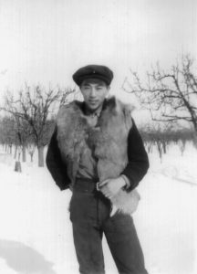 Dick Uyede standing outside in the winter with trees behind him wearing a fur vest