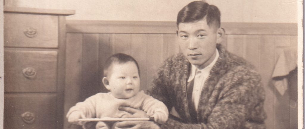 Man crouching holding an infant who is seated on a tricycle