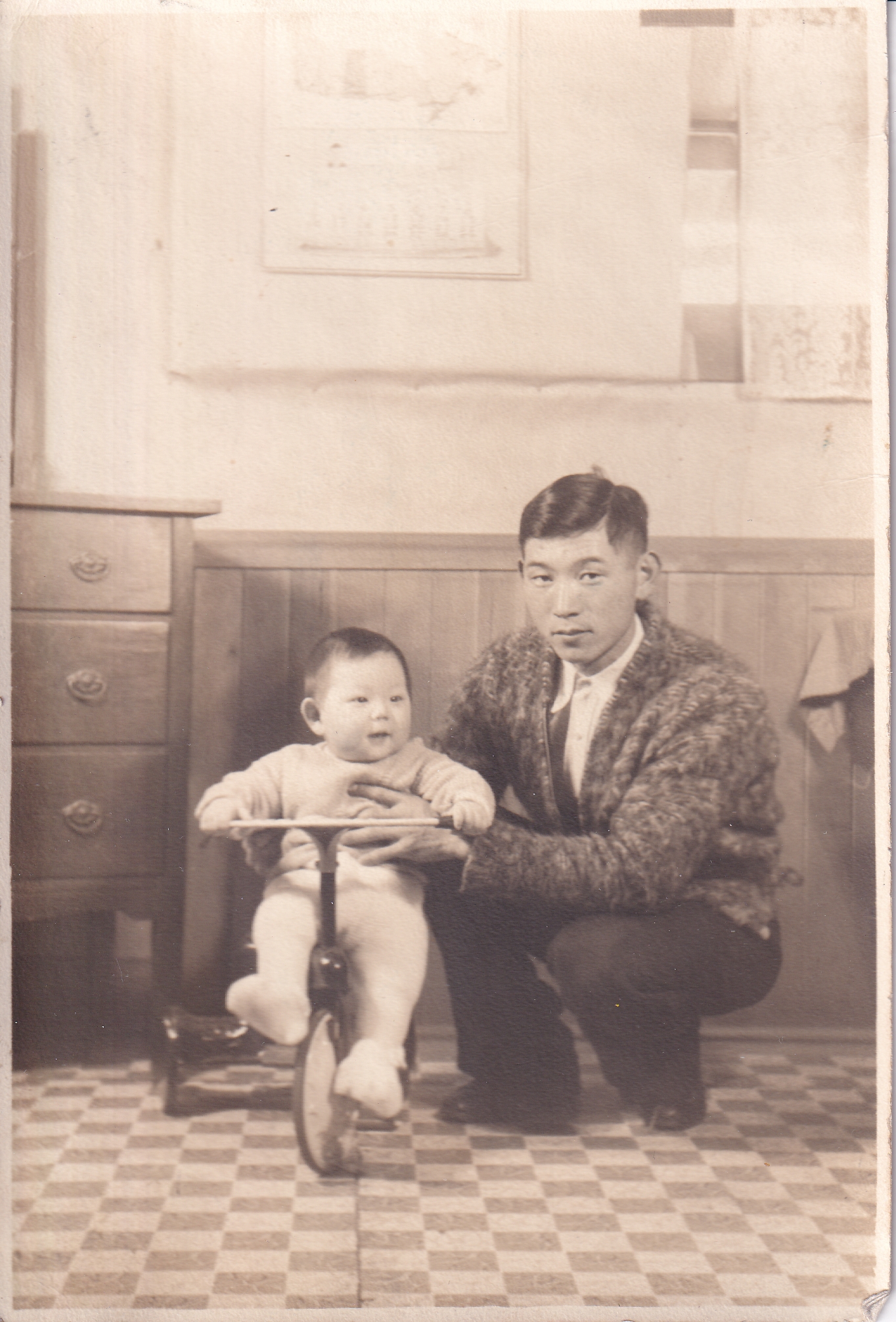 Man crouching holding an infant who is seated on a tricycle