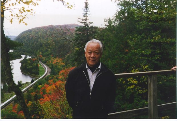 Jack Kobayashi standing outside with trees and a river below in a valley