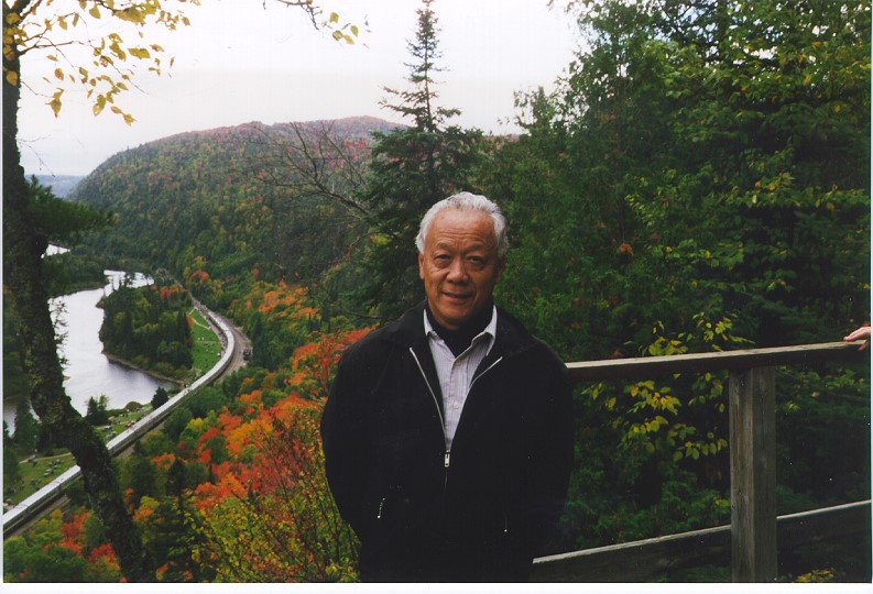Jack Kobayashi standing outside with trees and a river below in a valley
