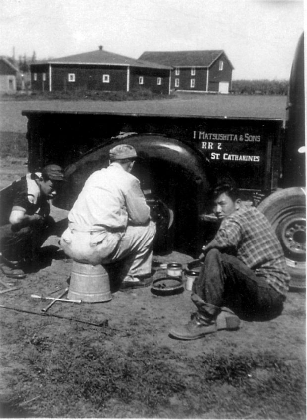 Three men beside the wheel of a truck fixing the tire