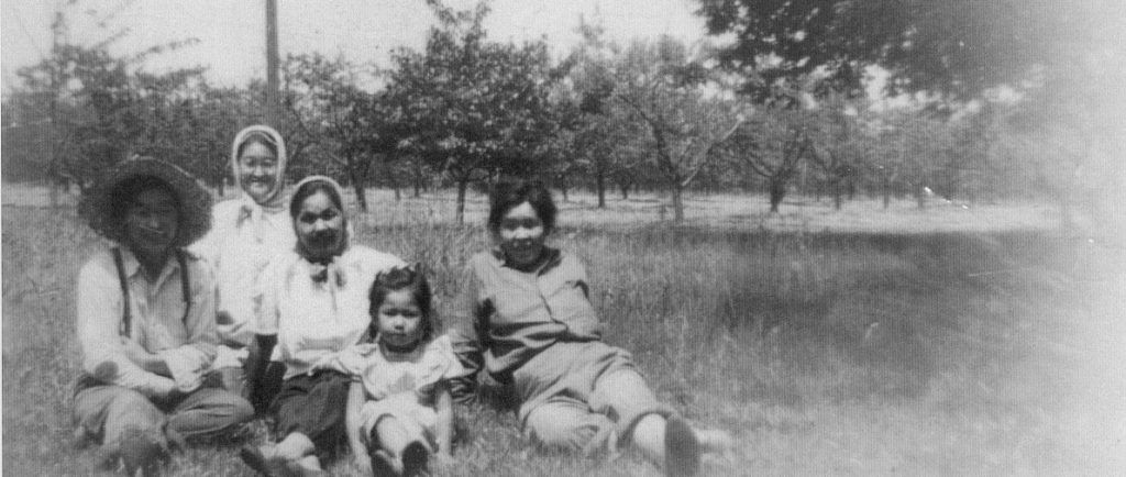 Four women and one girl seated together on the ground in an orchard