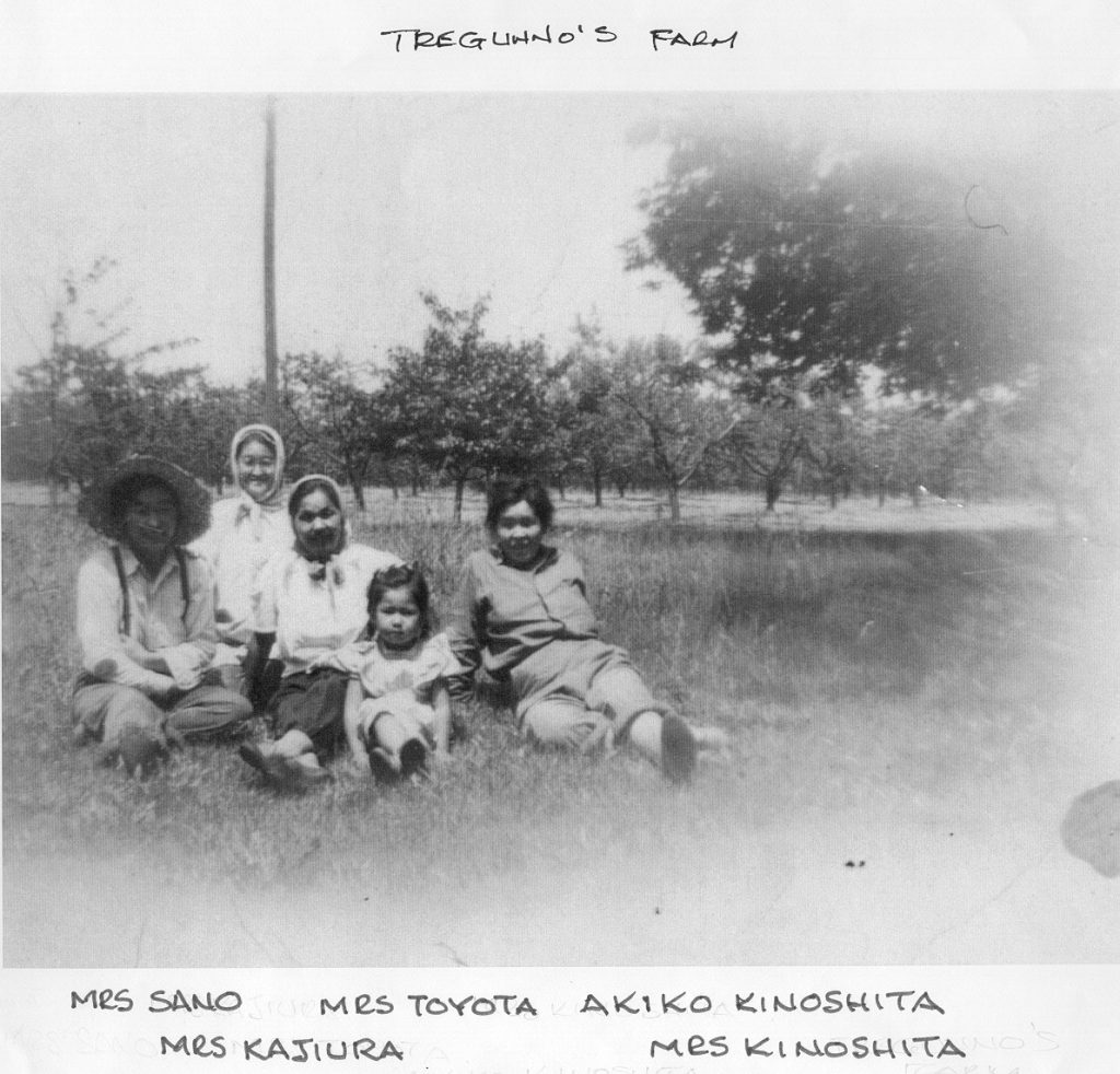 Four women and one girl seated together on the ground in an orchard