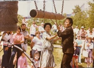 Woman and man swing a large pole to hit a bell