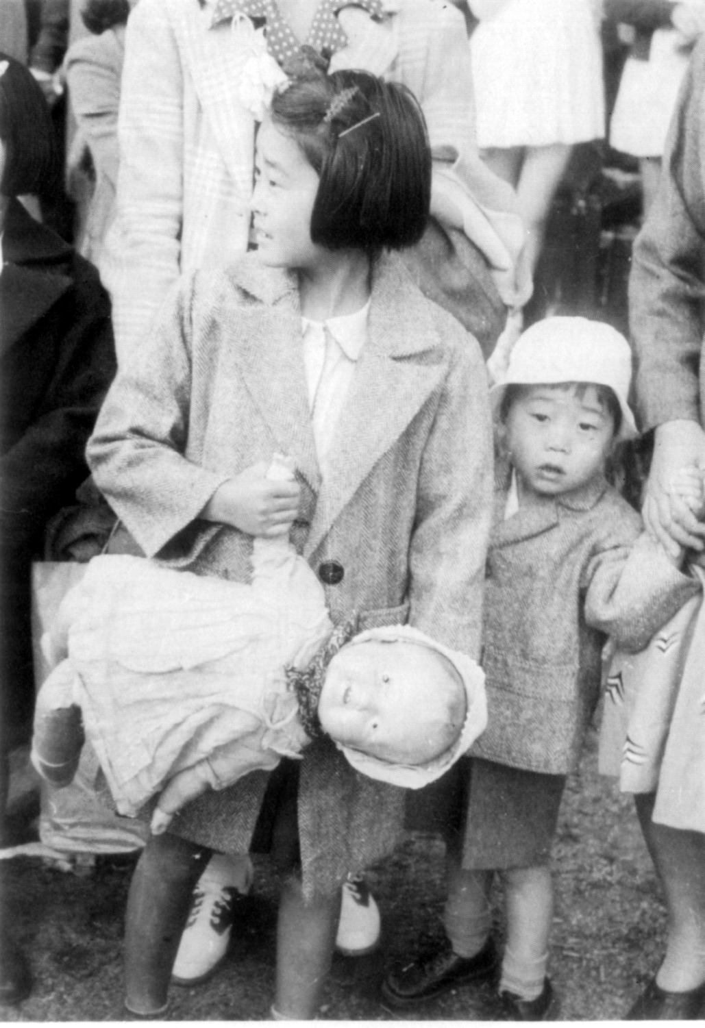 Young girl holding a doll and her younger brother's hand waiting to be exiled