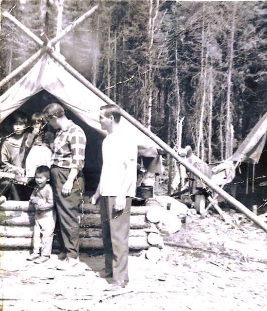 Anicinabek children and foreigners are in front of a bush camp.