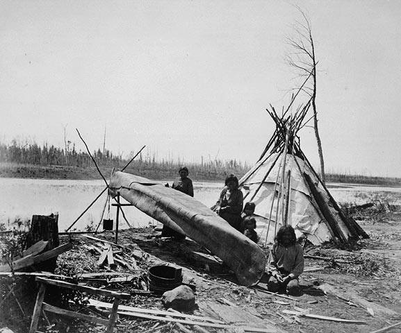 Summer camp, canoe making. The canoe building site is near a tent on the lake shore. Three adults and two children are seen here. Black and white picture.