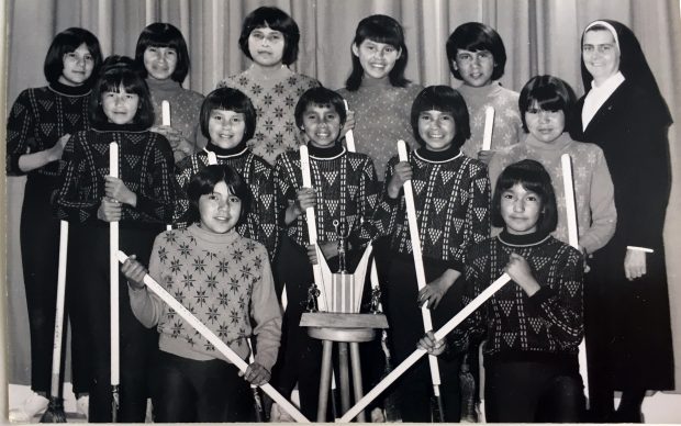 A women's broomball team at the Amos boarding school. Each of them holds her stick in her hands. A trophy is in the middle of the group and a sister is on the right. Black and white picture.