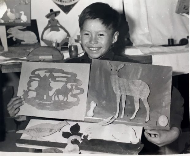 Young anicinabe presenting her artwork at the Amos boarding school. All smiles, he shows his engravings which represent animals in particular. Black and white picture.
