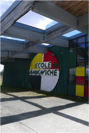 Front of the secondary school, Amik Wiche. We see its logo: a circle with four colors (red, yellow, white, black) and a beaver. Picture in color.