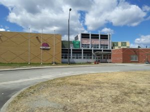 Front of the Lac Simon Elementary School. One portion is made of yellow bricks, the other of red bricks and a windowed portion in the center. We see a portion of the road that leads to the entrance. Picture in color.