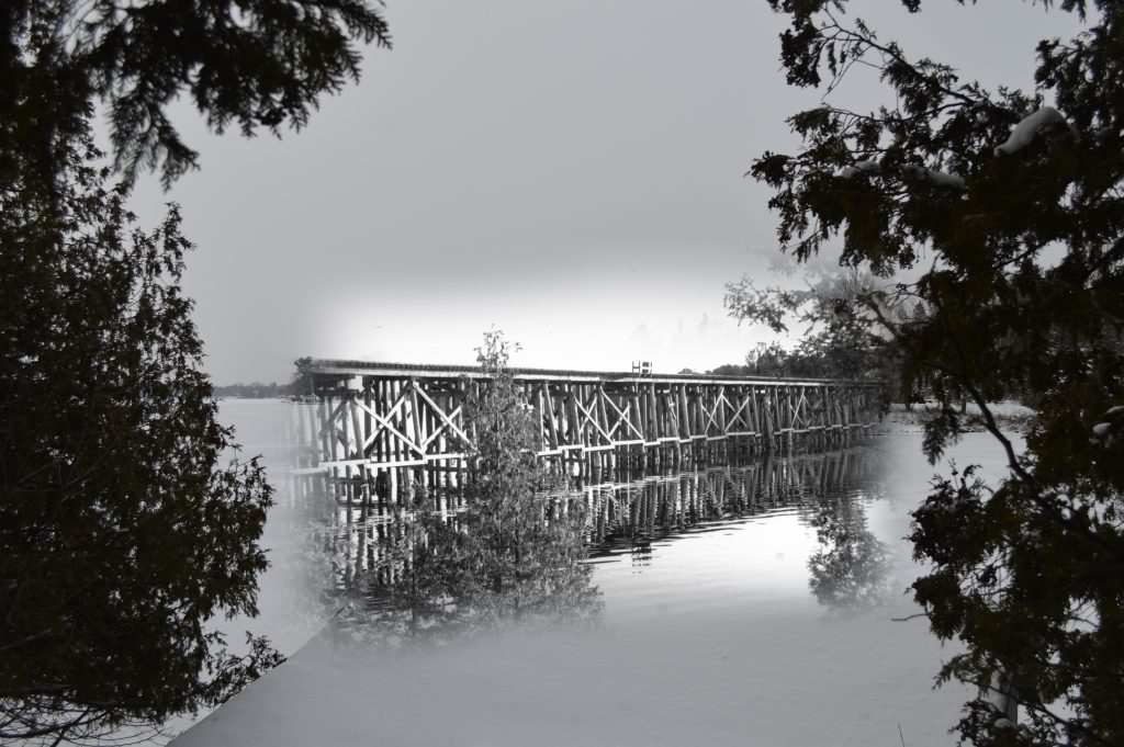 Une photo noir et blanc d' un pont à chevalets, superposée à une photo contemporaine d'un lac.