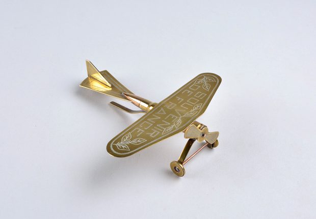 A small polished brass plane made from a bullet. It has one propeller in the front and has “Sourvenier de France.”