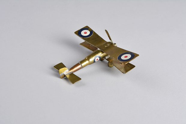A small polished brass plane made from a bullet. It has one propeller in the front and has targets painted on each wing and on the body.