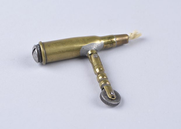 A rustic simple lighter with a hollowed bullet with a wick out its end. A bendable arm brings flint close to the wick.