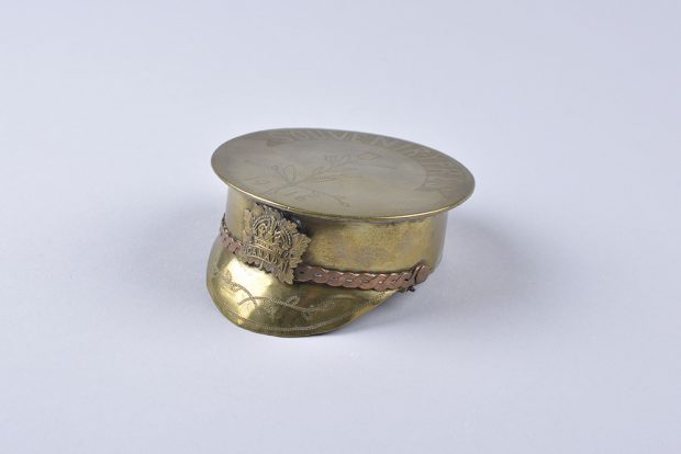 An ashtray in the shape of a detailed rimmed soldier cap with a brass Canada crest in the shape of a maple leaf on its brim.