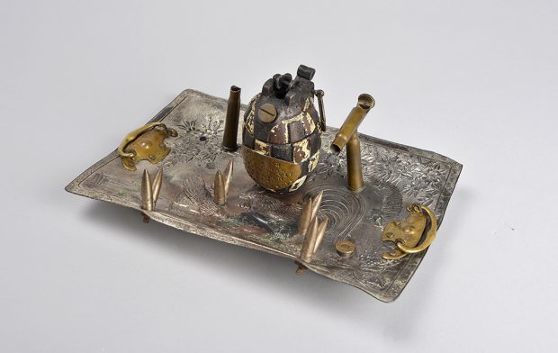 A dullened desk set made from many metals. It has a hand grenade in the middle surrounded by shell casings as pen holders.