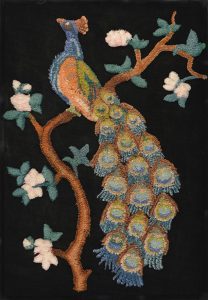 Broderie d’un paon très coloré, perché sur une branche feuillue avec des fleurs blanches.