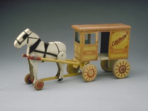 A wooden toy carving of a horse drawing a dairy carriage. The dairy carriage is painted a dull yellow, orange and red.