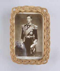 A hand weaved wicker frame around a black and white picture of King George VI in full uniform.