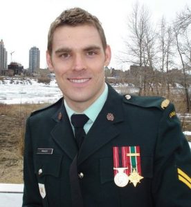 Colour contemporary photograph of a soldier in uniform without his cap. He is smiling at the camera and standing outside in late winter just before ice flow.