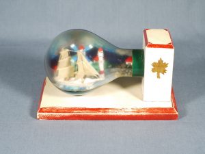A lightbulb containing a sailing ship model and a port scene complete with windmill and lighthouse. It is on a wooden mount.