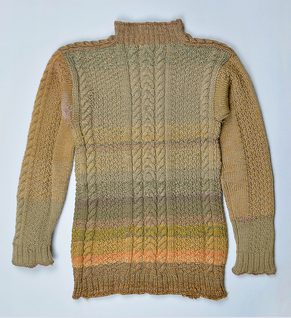 A handmade cable knit made of earth tone-colored wool. It is mostly moss green.