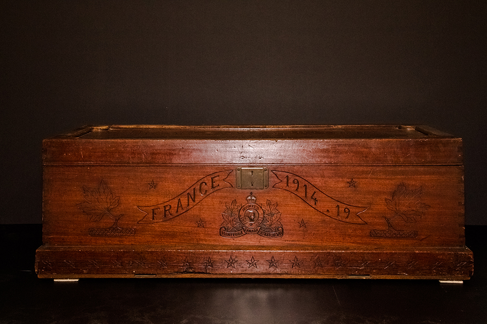 A photograph of the front of a handmade wooden footlocker showing engraving of and a brass plate lock.