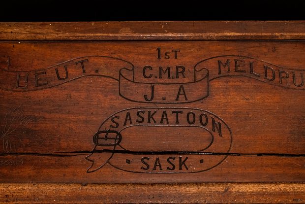 A detail photograph of a handmade wooden footlocker showing engraving of the owner’s name and city or origin.