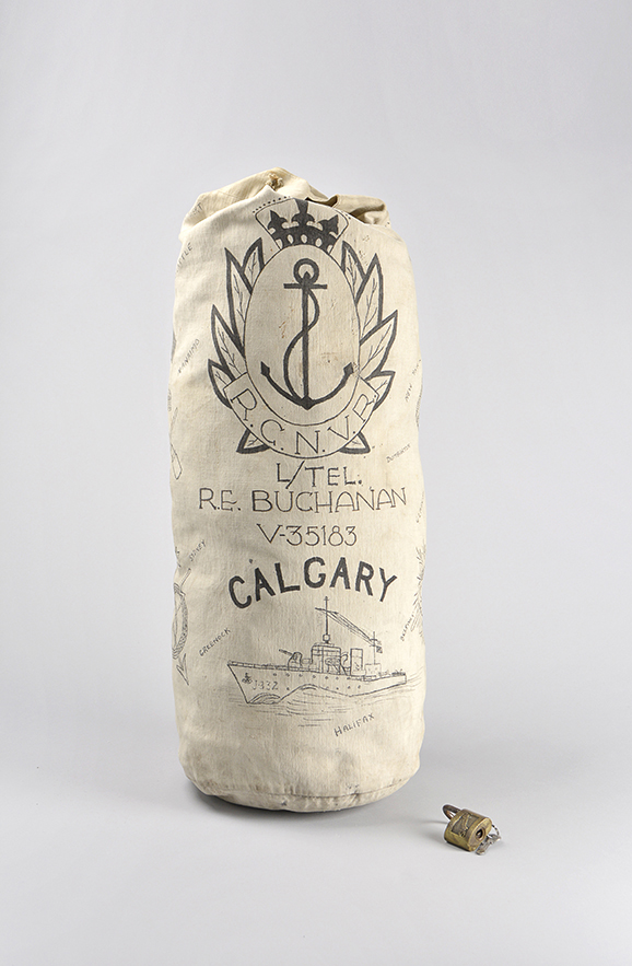 A cream-coloured canvas navy kit bag with a hand-drawn Royal Canadian Naval Volunteer Reserve logo above a soldier’s name and an image of a ship at sea.