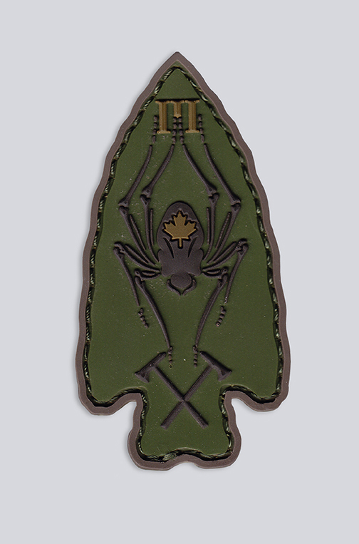 An arrow-shaped customized green patch with the tip pointing upward. It depicts an “M” at the top, a spider with a maple leaf on its abdomen in the middle and two cycles on the bottom.