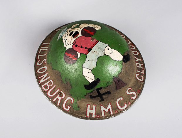 A helmet painted with a colour image of a fighting bulldog superimposed over a tree with a swastika being stomped under his foot. Three place names are painted in the lip of its outer rim.