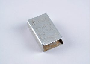 An aluminum matchbox cover hand engraved with place names.