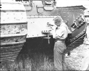 A black and white photo of a man in civilian clothes painting a crest on a Canadian tank.
