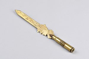 A letter opener made with polished brass. The handle is a shell casing and the attached blade is engraved with the word Amiens and is shaped with a soldier’s profile where it meets the casing.